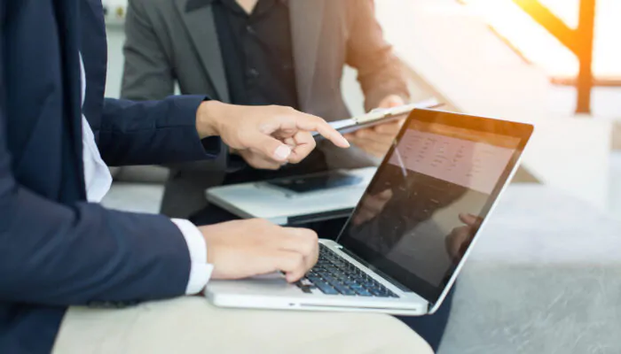 Two businessmen, one with a laptop on his lap, one holding a clipboard.