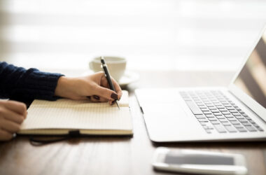 Close up of woman writing notes on her diary with laptop on table
