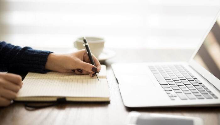 Close up of woman writing notes on her diary with laptop on table